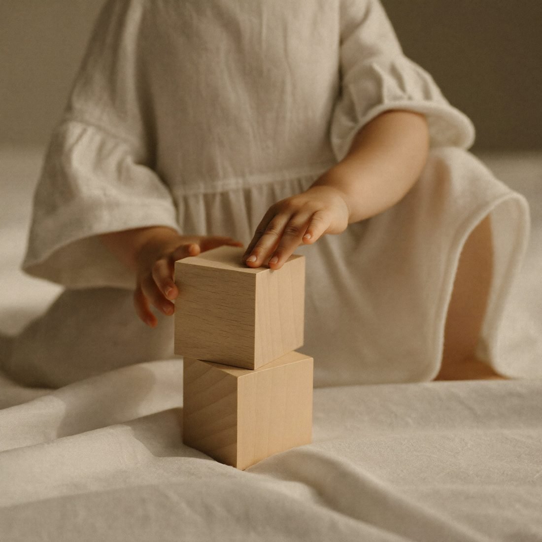 Mains d'un jeune enfant empilant des cubes en bois sur un tapis de lin
