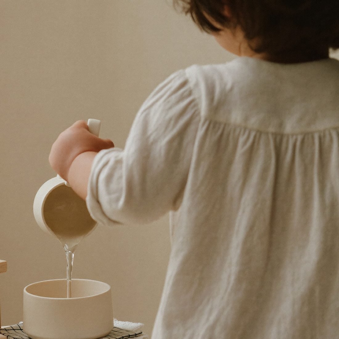 Enfant de dos versant de l'eau d'un petit pichet dans un verre