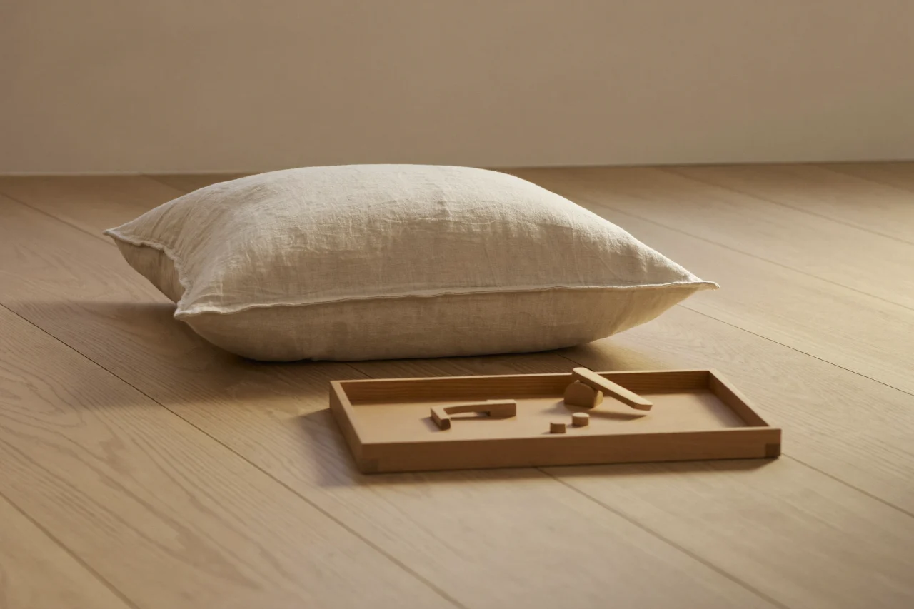 Coussin de lin posé au sol devant un plateau de bois clair garni de quelques pièces à manipuler