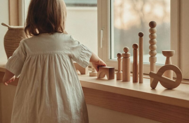 Étagère basse en bois avec quelques jouets Montessori rangés par tranche d'âge