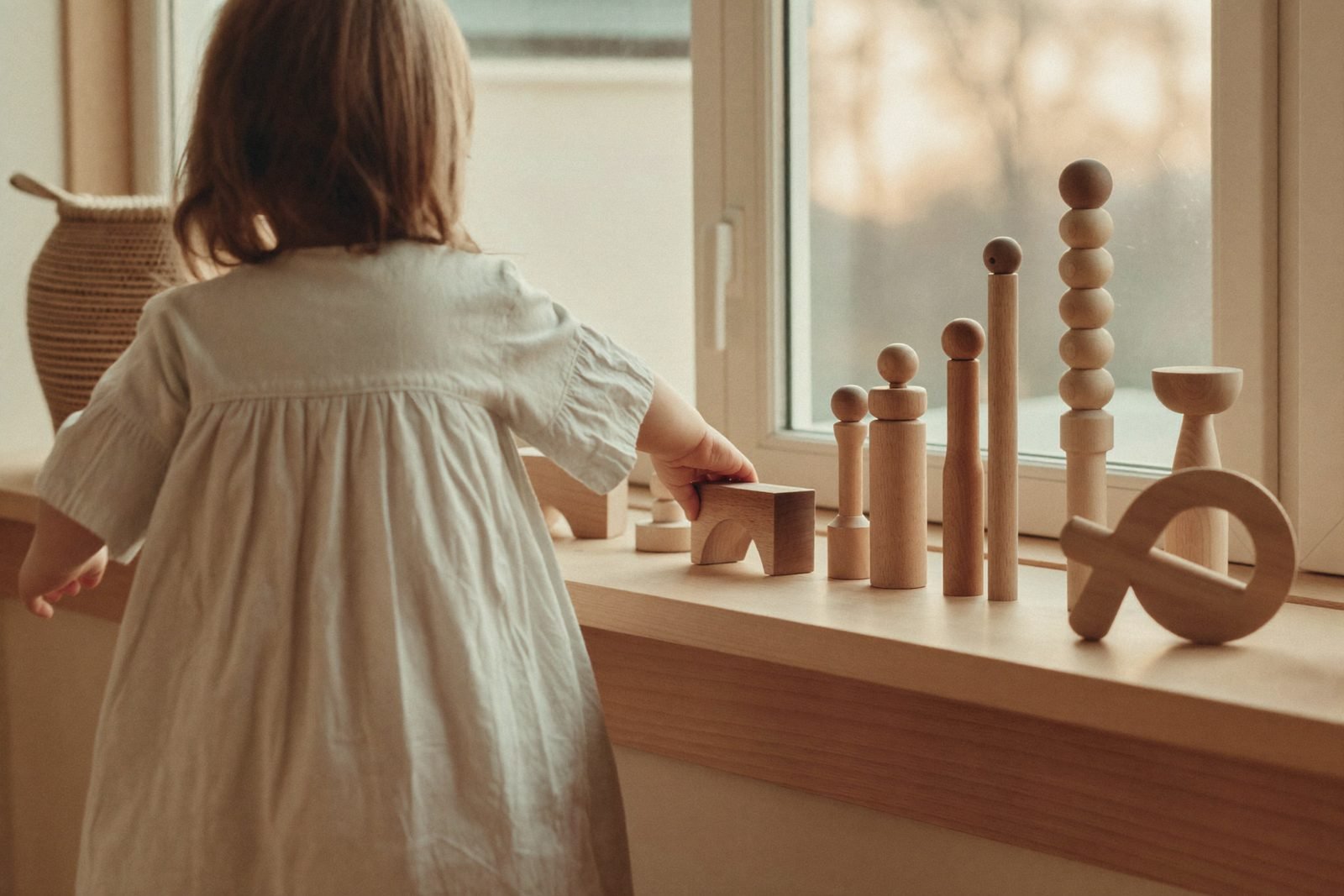 Étagère basse en bois avec quelques jouets Montessori rangés par tranche d'âge