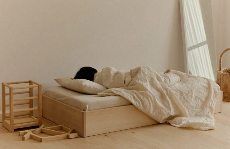 Lit au sol en bois clair avec couette pliée, dans une chambre épurée