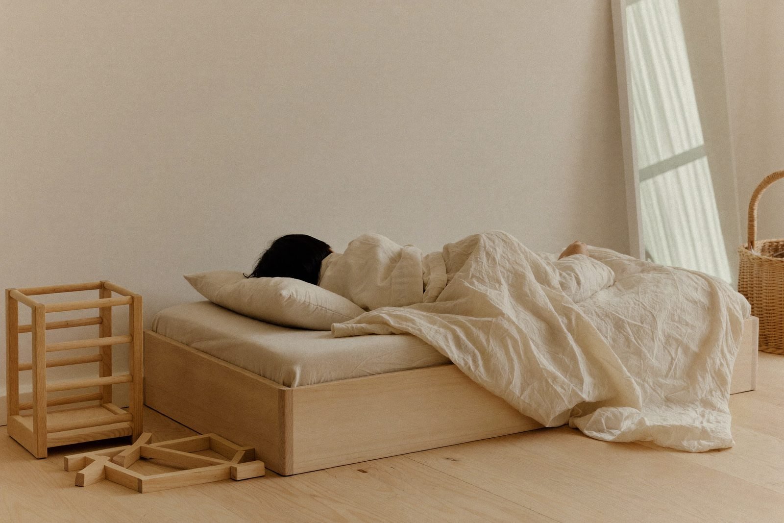 Lit au sol en bois clair avec couette pliée, dans une chambre épurée
