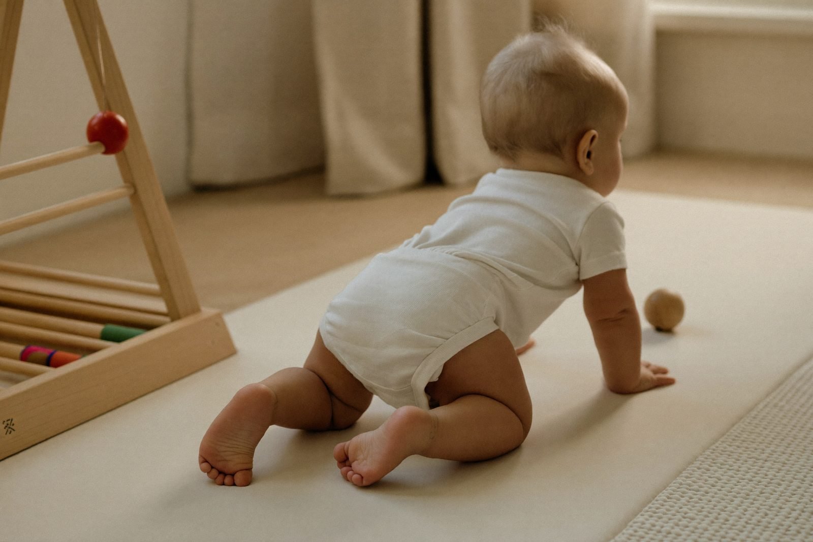 Bébé sur le ventre sur un tapis ferme, en train de tendre le bras vers un objet